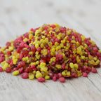 Gros plan sur un monticule de grains d'encens de résine Nazareth, montrant un mélange vif de couleurs rouge, rose fuchsia et jaune doré, sur une surface en bois clair.