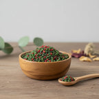 Grains d'encens de résine Nazareth Vert, mélange dominant de vert foncé et de rouge, dans un petit bol en bois avec cuillère, sur une surface en bois rustique.