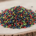 Gros plan sur un monticule de grains d'encens de résine Notre-Dame des Miracles, présentant un mélange très dense et varié de couleurs vives (bleu, rouge, vert, jaune, noir).