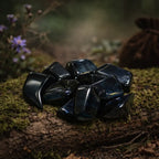 Un groupe de pierres d'œil de faucon roulées aux reflets bleu profond et chatoyants, disposé sur une branche moussue dans une ambiance de sous-bois.