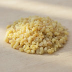 Gros plan sur un monticule de grains de résine d'Encens Oliban (Larmes d'Encens), montrant une couleur jaune pâle et ivoire, translucide, sur une surface en bois clair.
