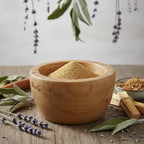 Palo santo en poudre pour fumigation, fine poudre dorée dans un mortier en bois entouré de sauge, lavande et bâtons de palo santo.