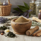 Poudre de patchouli finement moulue dans un mortier en bois, entourée d’herbes séchées, résines et bâtons de palo santo.