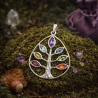 Pendentif en argent en forme de goutte représentant un arbre de vie dont les feuilles sont serties de 7 pierres naturelles colorées, posé sur de la mousse forestière.