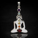 Un pendentif Bouddha en argent représentant les 7 chakras par l'alignement vertical de sept pierres naturelles de couleurs différentes, présenté sur un fond noir avec un reflet net.