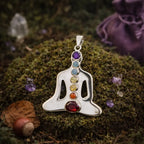 Pendentif en argent représentant un Bouddha en méditation serti de 7 pierres naturelles colorées (violet, bleu, vert, jaune, orange, rouge), posé sur de la mousse forestière.