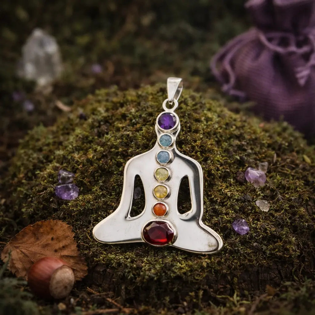 Pendentif en argent représentant un Bouddha en méditation serti de 7 pierres naturelles colorées (violet, bleu, vert, jaune, orange, rouge), posé sur de la mousse forestière.