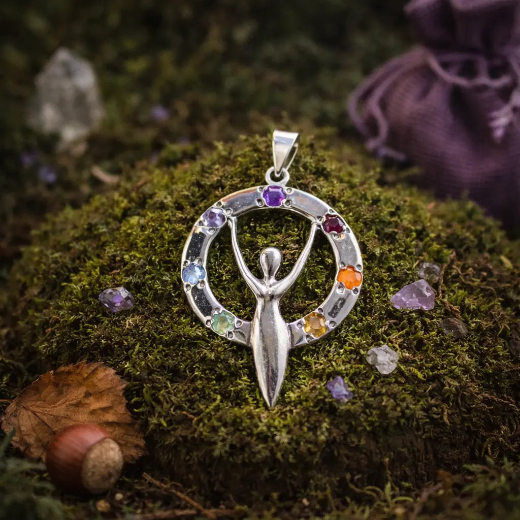 Pendentif en argent représentant une silhouette de déesse aux bras levés, entourée d'un cercle serti de 7 pierres naturelles colorées, posé sur de la mousse.
