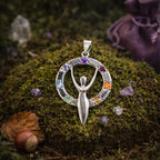 Pendentif en argent représentant une silhouette de déesse aux bras levés, entourée d'un cercle serti de 7 pierres naturelles colorées, posé sur de la mousse.