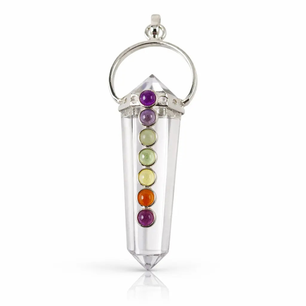 Un pendentif 7 chakras composé d'une pointe de cristal de roche taillée, ornée de sept petites pierres multicolores alignées et d'une monture en métal argenté, présenté sur un fond blanc.
