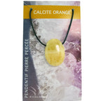 Un pendentif en calcite orange poli et percé, présentant une teinte jaune orangé douce et marbrée, monté sur un cordon noir et présenté sur son emballage cartonné illustré.