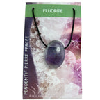 Un pendentif en fluorite poli et percé, affichant des teintes violettes et translucides, monté sur un cordon noir et présenté sur son emballage cartonné illustré.