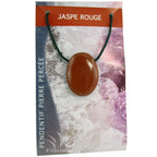 Un pendentif en jaspe rouge poli et percé, d'une couleur rouge brique opaque et uniforme, monté sur un cordon noir et présenté sur son emballage cartonné illustré.