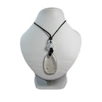 Un pendentif en cristal de roche taillé en forme de goutte translucide, orné d'une petite perle argentée et d'une bille de cristal, présenté sur un buste d'exposition blanc.
