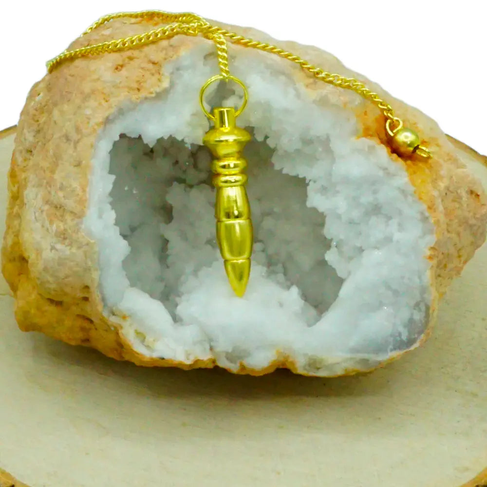 Pendule égyptien du Nil en métal doré brillant, suspendu par sa chaîne devant l'ouverture d'une géode de cristaux blancs.