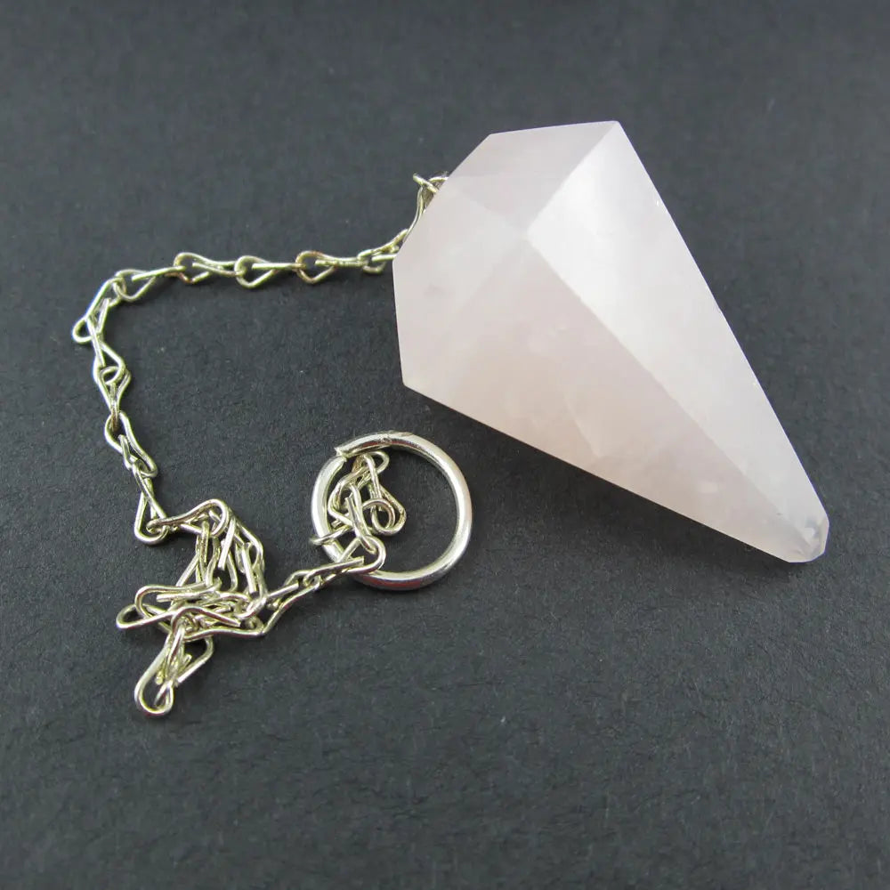 
Pendule en quartz rose taillé en cône à facettes avec chaîne en métal argenté et anneau terminal posé sur un fond noir.