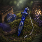 Pendule égyptien Thot en lapis lazuli bleu nuit pailleté de pyrite dorée, posé sur un lit de mousse moussue à côté d'une pierre brute, d'un livre ancien et d'une lumière tamisée.