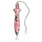 Pendule Thot rhodonite en pierre naturelle rose marbrée de noir, sculpté de motifs géométriques et suspendu à une chaîne en métal argenté dotée d'une perle transparente.