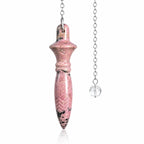 Pendule Thot rhodonite en pierre naturelle rose veinée de noir, sculpté de gravures géométriques, suspendu à une chaîne métallique argentée munie d'une perle en verre transparent.