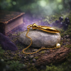 Pendule de radiesthésie Nil en laiton doré avec chambre à témoin et perle nacrée, posé sur une pierre blanche au cœur d'une forêt mystique.