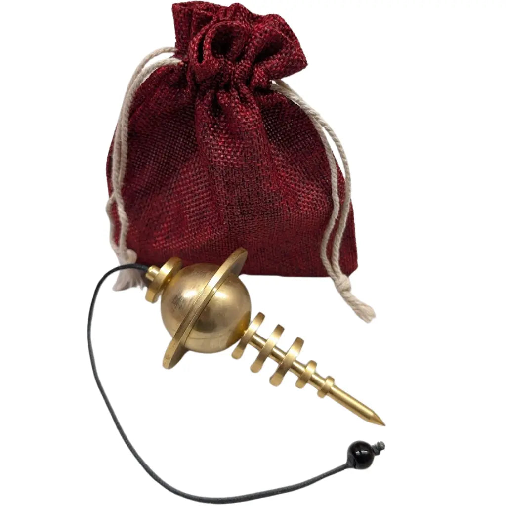 Pendule Planétaire doré en métal avec sphère et anneau posé devant une pochette en tissu rouge.