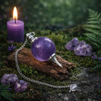 Pendule Sephoroton en Améthyste violette avec monture argentée posé sur une écorce de bois dans une atmosphère rituelle mystique avec bougie pourpre.