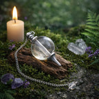 Pendule Sephoroton en Cristal de roche translucide avec monture argentée posé sur une écorce ancienne dans une atmosphère rituelle lumineuse.