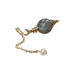 Pendule Séphoroton en labradorite aux reflets bleutés avec monture et chaîne en métal doré, terminé par une perle blanche sur fond blanc.
