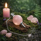 Pendule Sephoroton en Quartz Rose avec monture argentée posé sur une écorce de bois dans une ambiance rituelle douce avec bougie rose et cristaux.