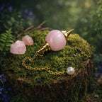 Pendule Sephoroton en Quartz Rose sphérique rose pâle avec monture dorée, posé sur un lit de mousse forestière avec des éclats de cristal rose et une lumière naturelle douce.