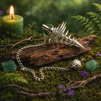 Pendule en spirale de laiton argenté avec perle ciselée posé sur un bois ancien dans une ambiance de forêt mystique avec bougie et cristaux.