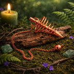 Pendule en spirale de laiton cuivré avec perle lisse posé sur un bois ancien dans une ambiance de forêt mystique avec bougie et cristaux.