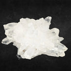 Amas de cristal de roche brut blanc aux multiples prismes naturels sur fond noir.