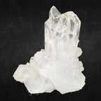 Amas de cristal de roche composé de plusieurs pointes de quartz transparentes sur un fond noir texturé.