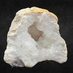 Cavité centrale d'une géode de quartz blanc avec amas de cristaux scintillants et croûte ocre sur fond noir.