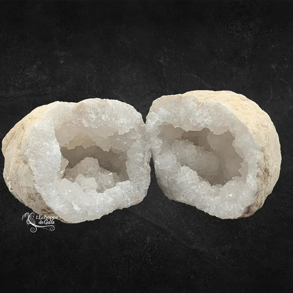 Une géode de quartz blanc ouverte en deux, révélant ses cristaux étincelants sur fond texturé noir.