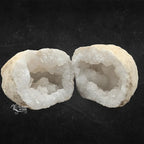 Une géode de quartz blanc ouverte en deux, révélant ses cristaux étincelants sur fond texturé noir.