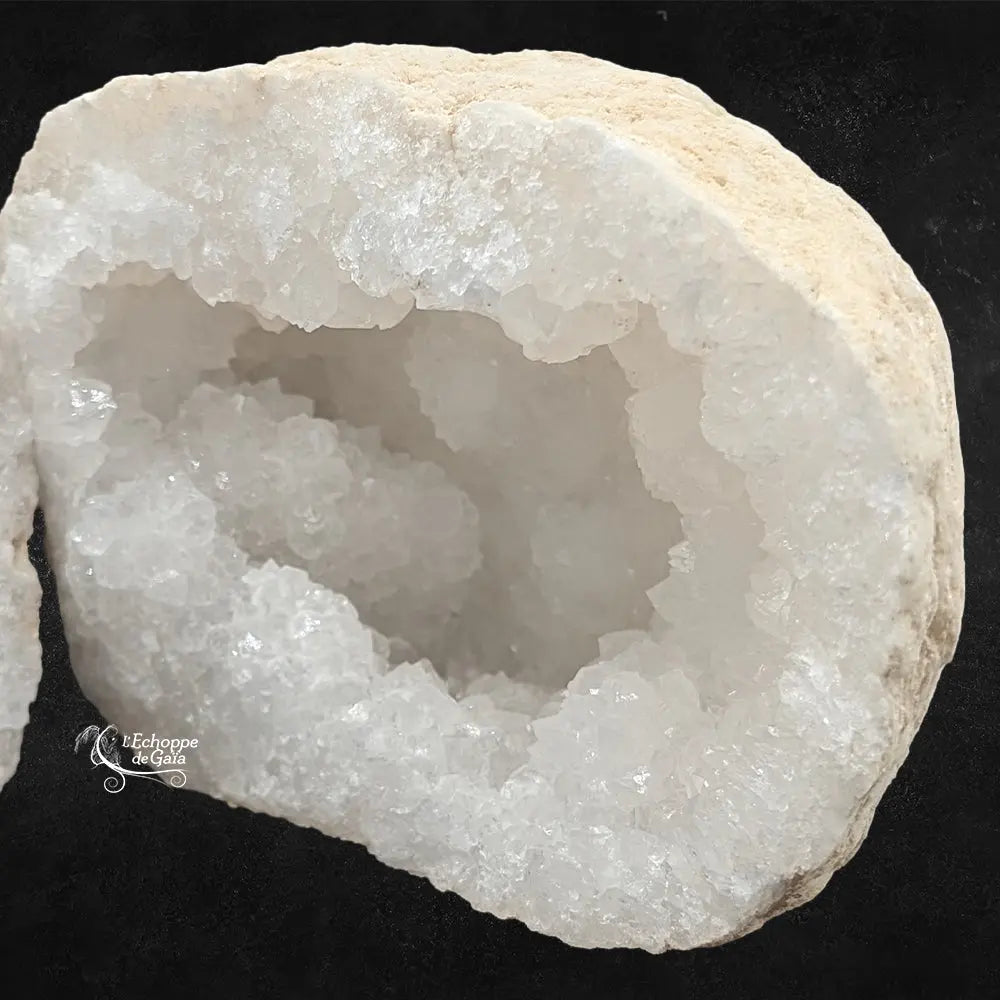 Zoom sur les cristaux intérieurs d'une géode de quartz blanc, texture rocheuse beige en bordure.