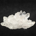 Amas de cristal de roche brut aux pointes cristallines bien définies sur fond noir mat.