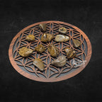 Plusieurs pierres de bronzite polies, aux teintes brunes et reflets métalliques dorés, disposées sur une fleur de vie en bois sur fond noir.