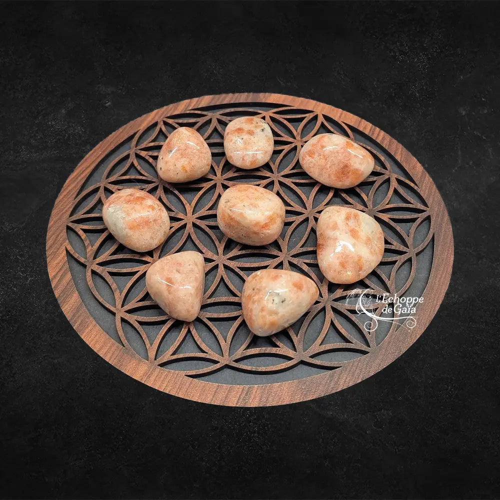 Pierres de soleil polies aux teintes orangées, disposées sur une fleur de vie en bois.