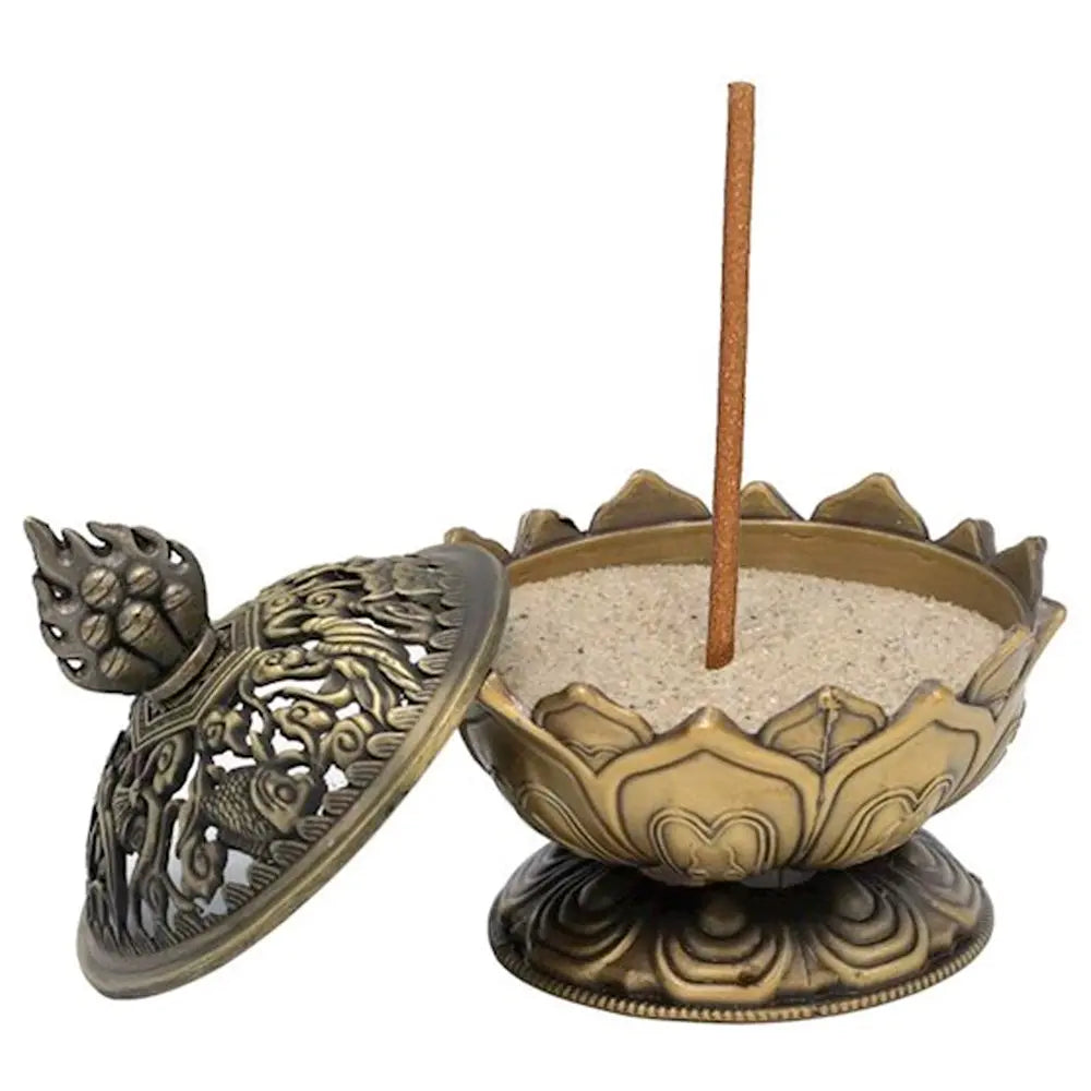 Porte-encens en forme de lotus en métal bronze, avec bol rempli de sable et bâton d’encens vertical, couvercle ajouré posé à côté, sur fond blanc.