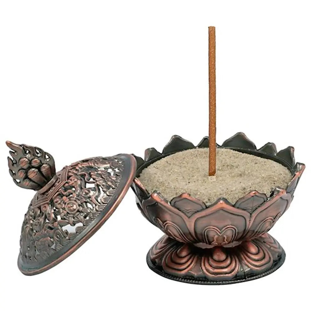 Porte-encens tibétain en forme de lotus finition cuivre, avec bol rempli de sable et bâton d’encens vertical, couvercle ajouré posé à côté, sur fond blanc.