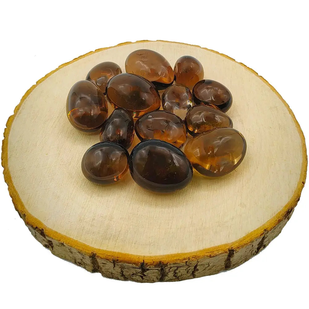 Un groupe de pierres de quartz fumé roulées aux nuances brunes et ambrées translucides, disposé sur une rondelle de bois clair.