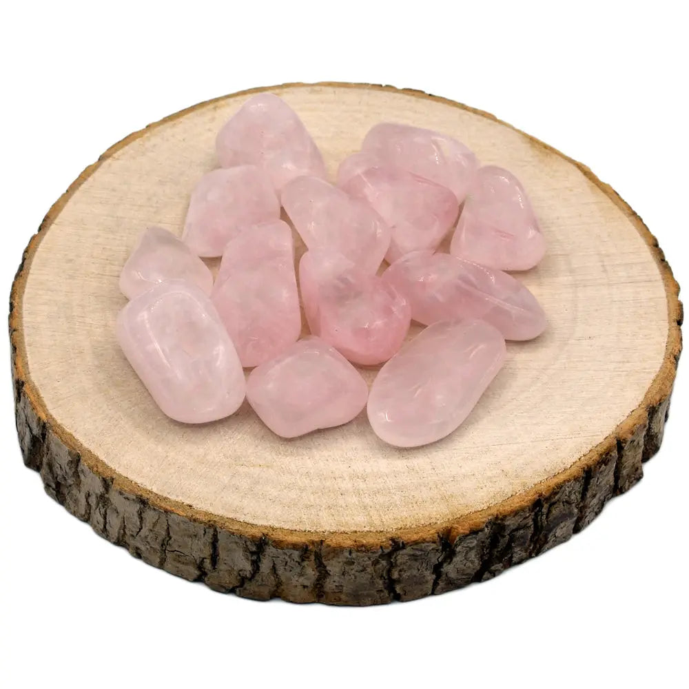 Un groupe de pierres de quartz rose roulées de qualité A, offrant une belle transparence et une teinte rose pastel uniforme, présenté sur une rondelle de bois naturel.
