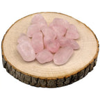 Un groupe de pierres de quartz rose roulées de qualité A, offrant une belle transparence et une teinte rose pastel uniforme, présenté sur une rondelle de bois naturel.