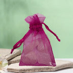 Un petit sac en organza rose fuchsia contenant des pierres de quartz rose, posé sur une pierre plate naturelle devant un arrière-plan vert clair.
