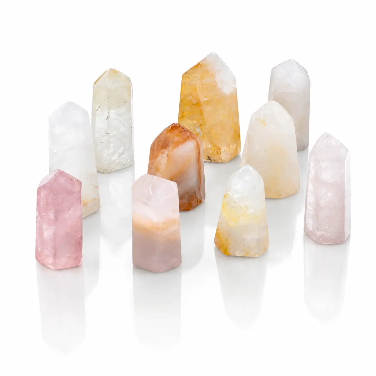 Plusieurs cristaux polis en forme de pointes de quartz hématoïde aux teintes blanches, roses et orangées sont disposés sur un fond blanc neutre.
