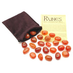 Set de runes en cornaline orange gravées dorées, avec pochette en velours marron et fiche d’information sur les runes.