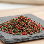Gros plan sur un monticule de grains d'encens de résine Saint Georges, mélange vibrant de couleurs rouge, vert et noir, posé sur une ardoise sombre.